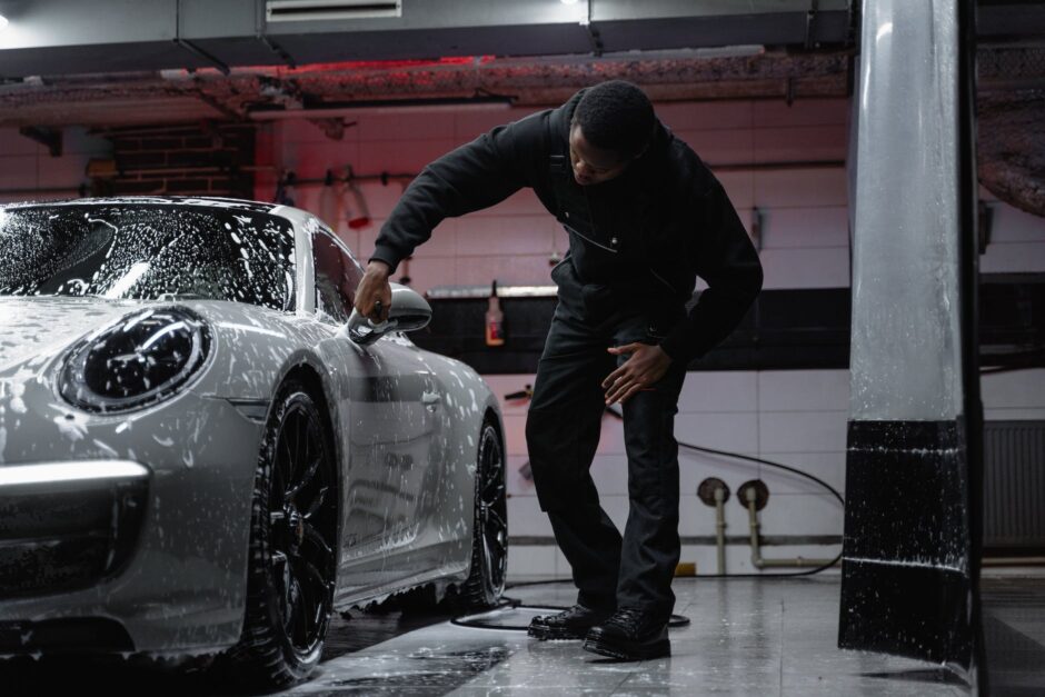 man in black jacket wiping the white car